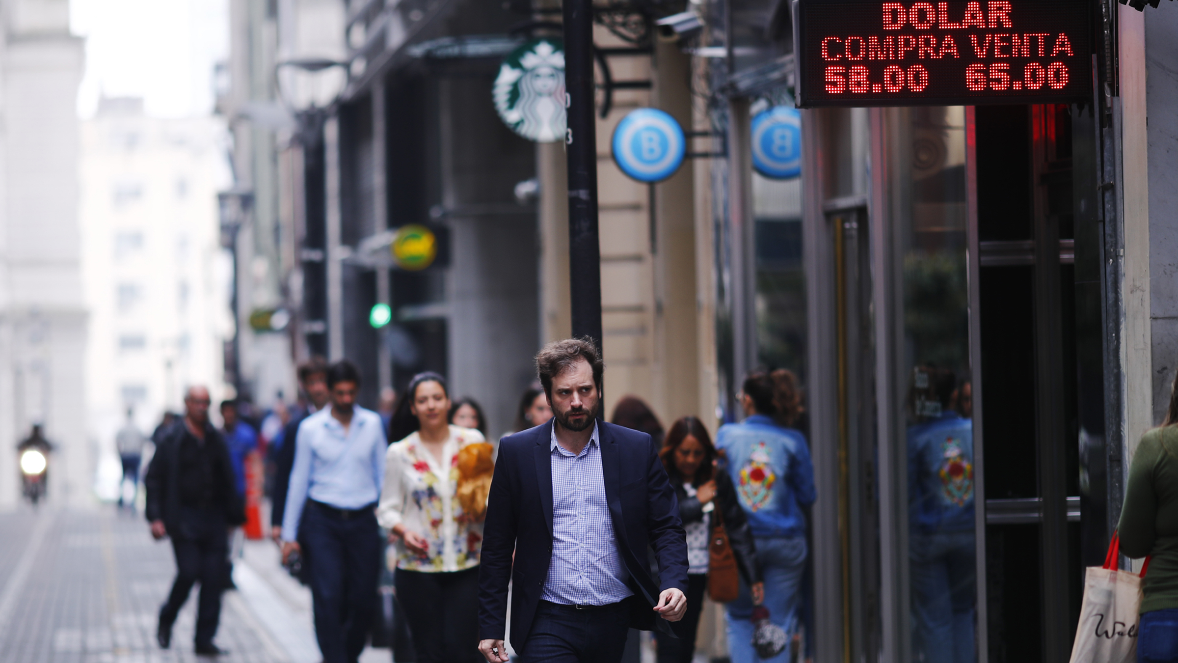 People walking down an Argentinian street with an exchange rate sign in the foreground