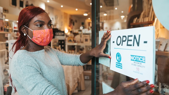 Small business owner applying an -OPEN- sign to the entrace door with the safety measures to respect during Covid-19 pandemic.