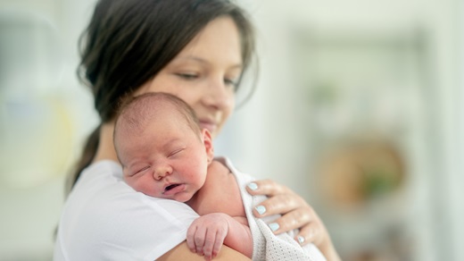 A newborn baby sleeps on mother's shoulder