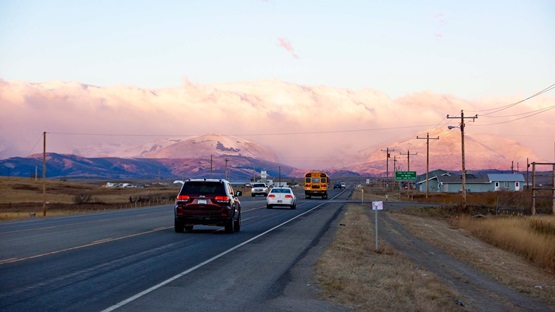 At dusk on a clear evening, cars travel along U.S. Highway 89 outside of Browning, Montana, on the Blackfeet Indian Reservation. The Rocky Mountains in Glacier National Park appear in the distance.