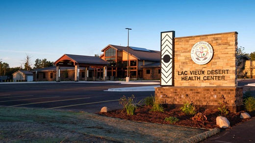 Exterior view of the Lac Vieux Desert Health Center building, taken at sunrise or sunset, with the center's sign in the foreground