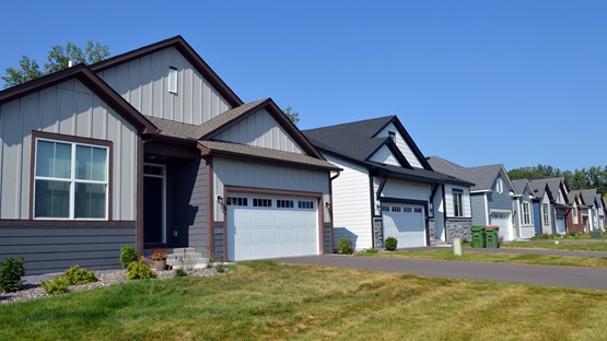 On a clear summer day, a row of small, newly constructed one-story single-family homes extends into the distance.