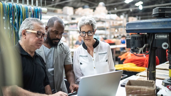 Image of factory workers of varied ages working together at a computer