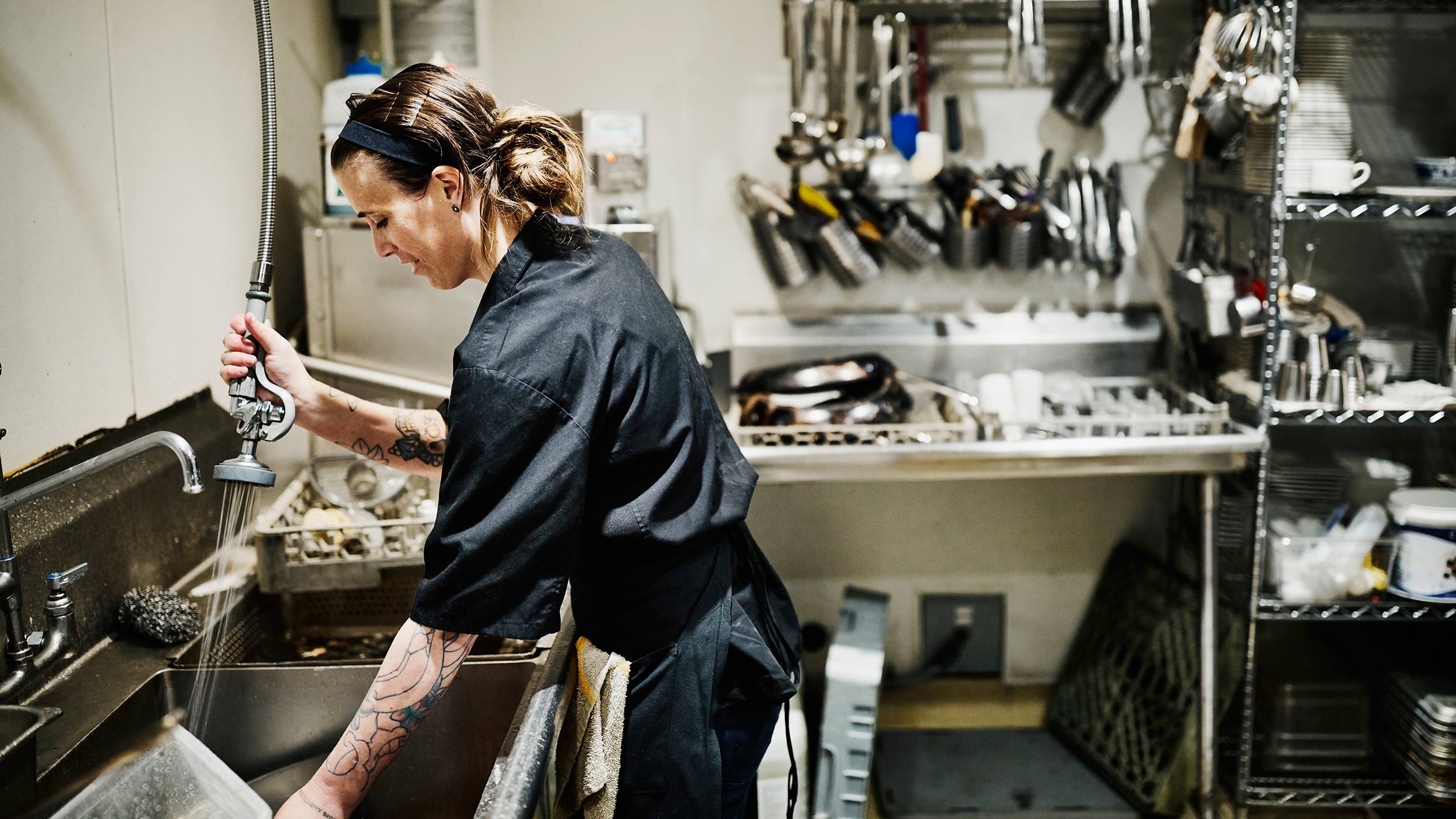 Woman with a ponytail in a black shirt washing dishes in a restaurant