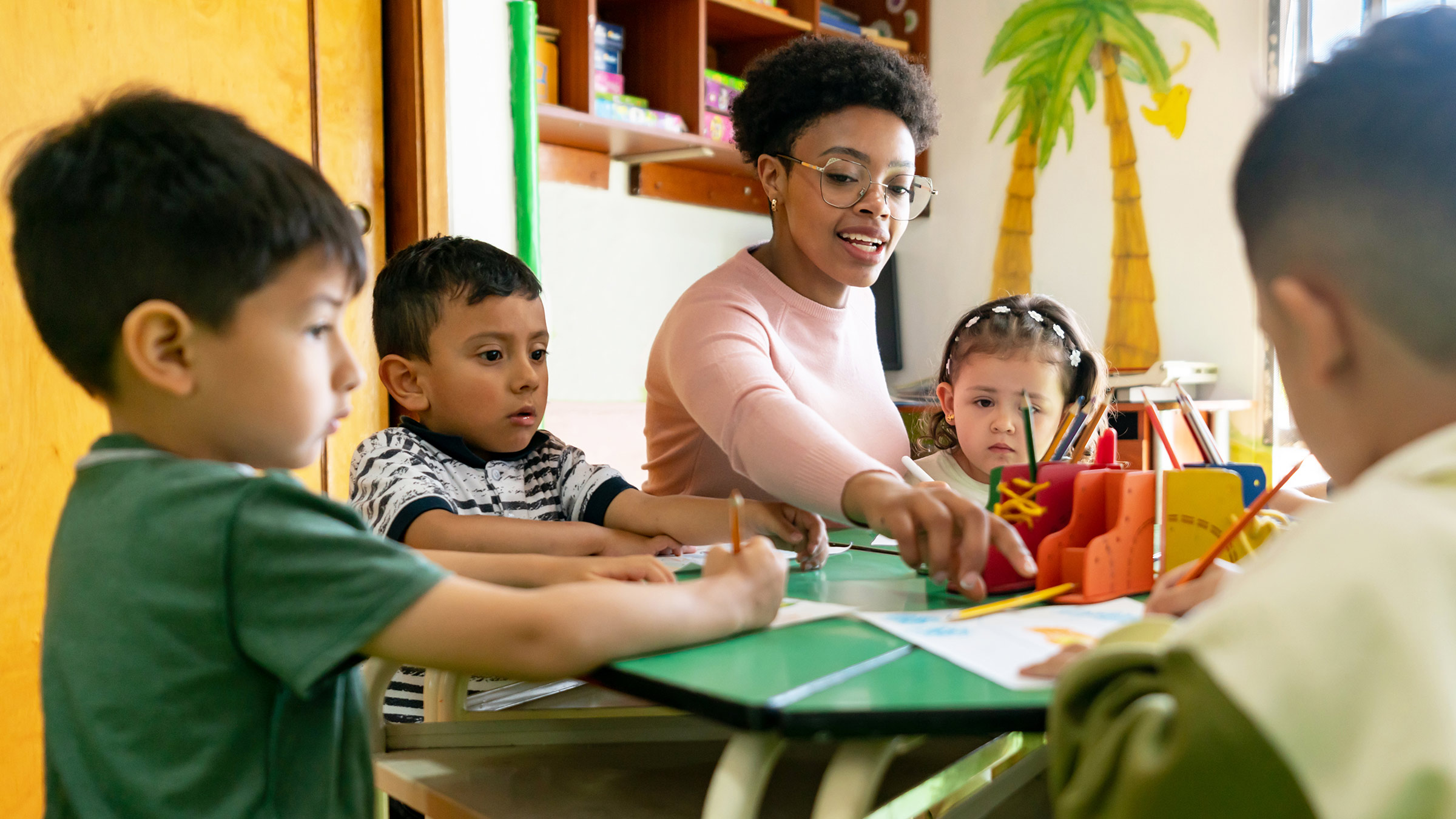Teacher supervising a group of preschoolers coloring in class at school