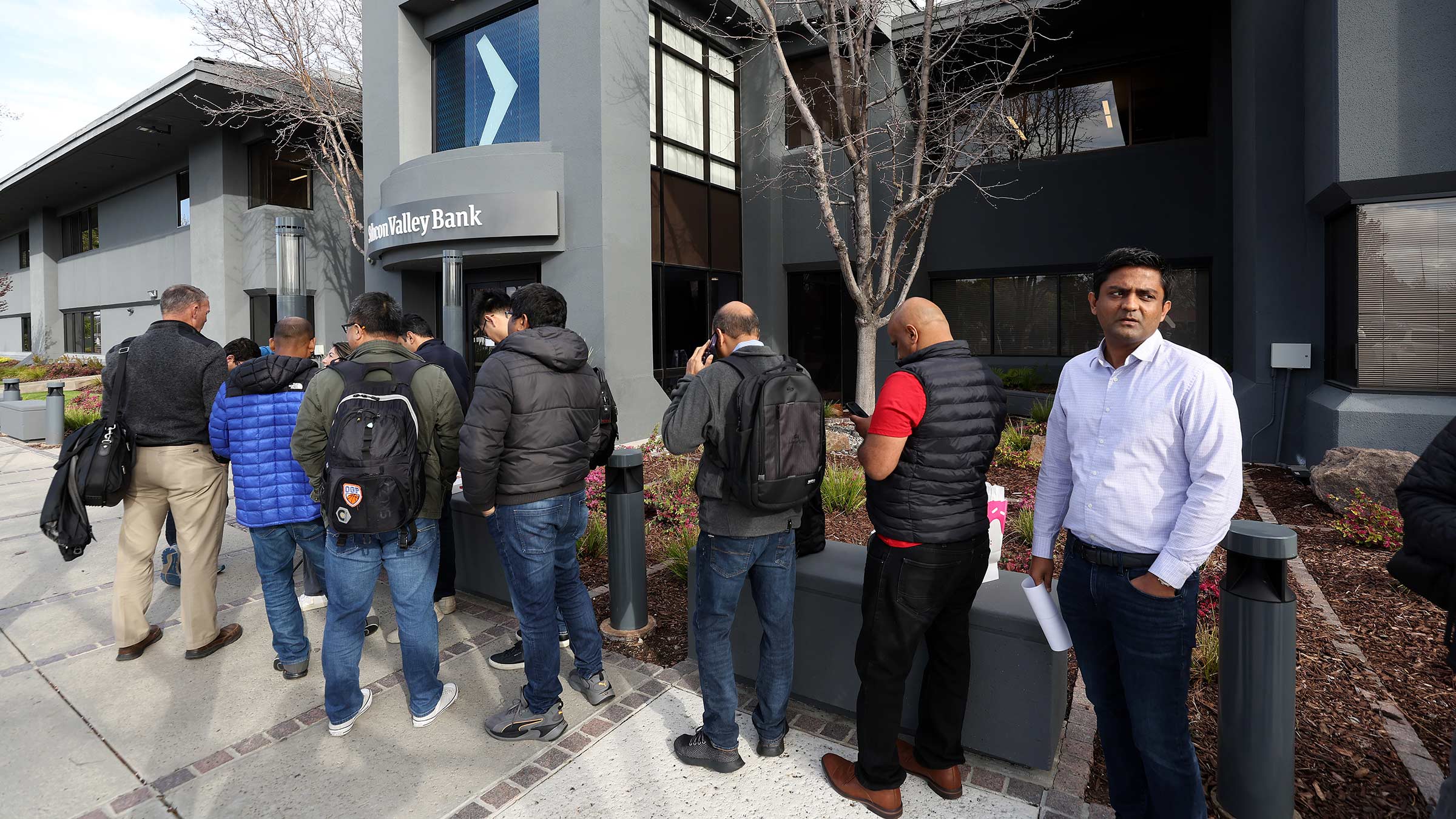 A line of bank customers wrapped around the outside of a bank waiting to withdraw from their accounts during a bank run