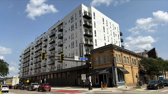 A view of Hencen Apartments in Minneapolis, shot from street level at the corner of 4th Street SE and Hennepin Avenue on a partly cloudy summer day.
